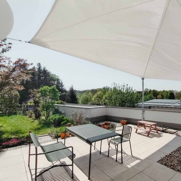 Großes weißes Sonnensegel über einer Terrasse mit modernen Metallgartenmöbeln und Blick in den Garten.