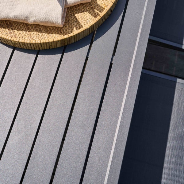 Nahaufnahme einer Gartentischoberfläche aus grauen Aluminiumlamellen mit einem geflochtenen Tablett und einem Tuch.