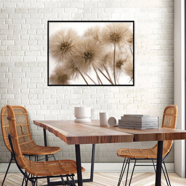 Gerahmtes Wandbild mit Pusteblumen-Motiv an einer Ziegelwand über einem massiven Holztisch und Rattanstühlen.