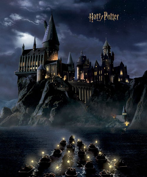 Nachtansicht von Schloss Hogwarts mit dem Harry Potter Logo darüber, beleuchtet von Booten auf einem See