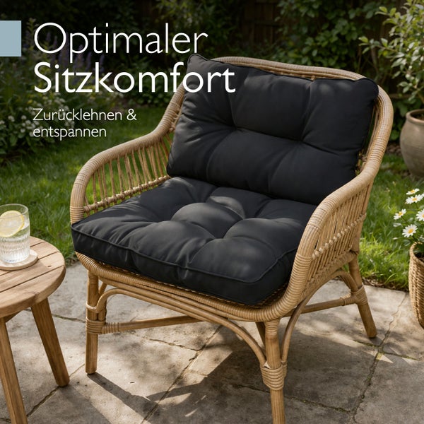 Garten-Sessel aus Rattan-Geflecht mit dicken dunklen Sitz- und Rückenkissen auf einer Terrasse im Garten.