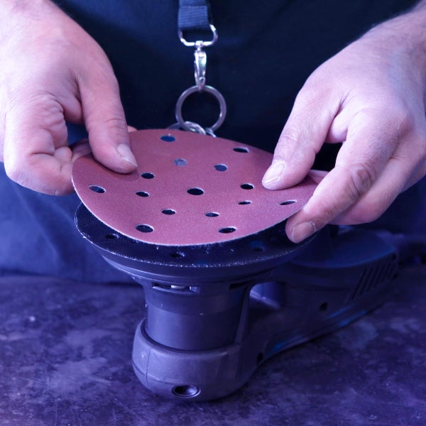 Eine Person befestigt ein Schleifpapier an einem Exzenterschleifer.