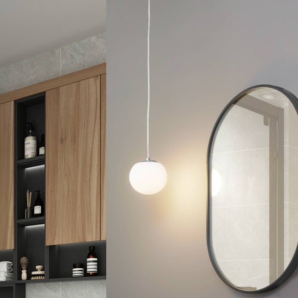 Moderne Pendelleuchte mit weißem, kugelförmigem Schirm in einem Badezimmer neben einem ovalen Spiegel und einem Holzschrank.