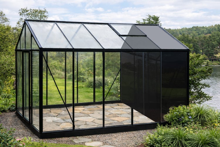 Modernes Gewächshaus mit schwarzem Rahmen und Glaspaneelen, teils mit Schattiernetz bedeckt, auf einer Steinterrasse im Garten.