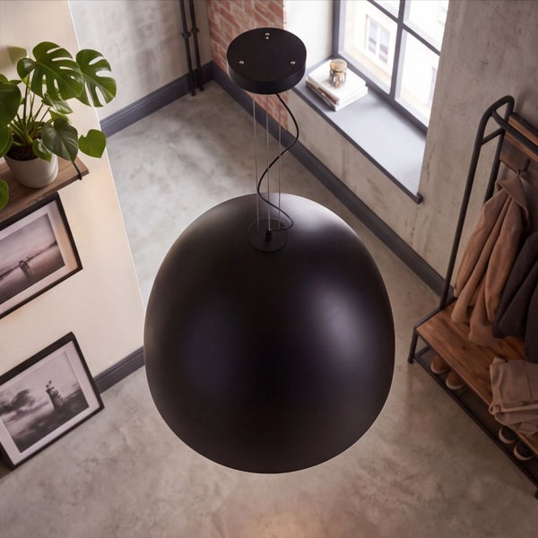 Moderne schwarze kugelförmige Pendelleuchte in einem industriell gestalteten Raum mit Betonboden, Garderobe und Zimmerpflanze.