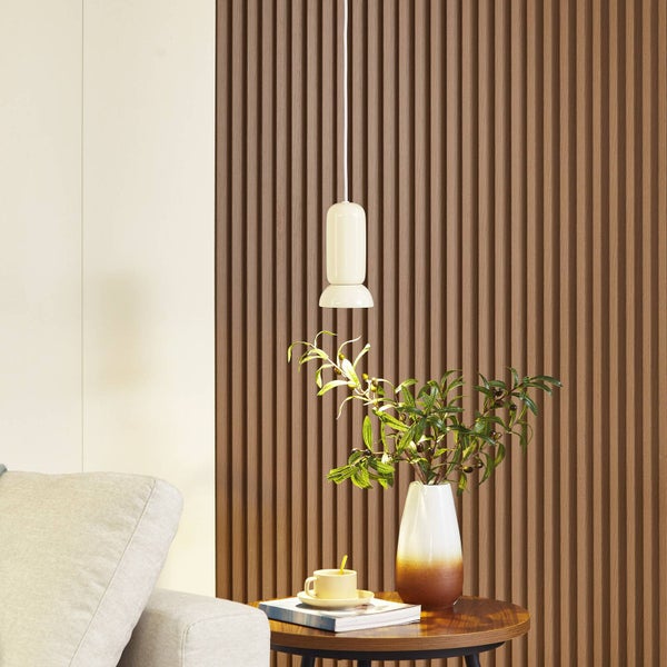 Akustikpaneel in Holzoptik mit vertikalen Lamellen hinter einem Beistelltisch mit Vase und einer Hängeleuchte in einem hellen Wohnraum.