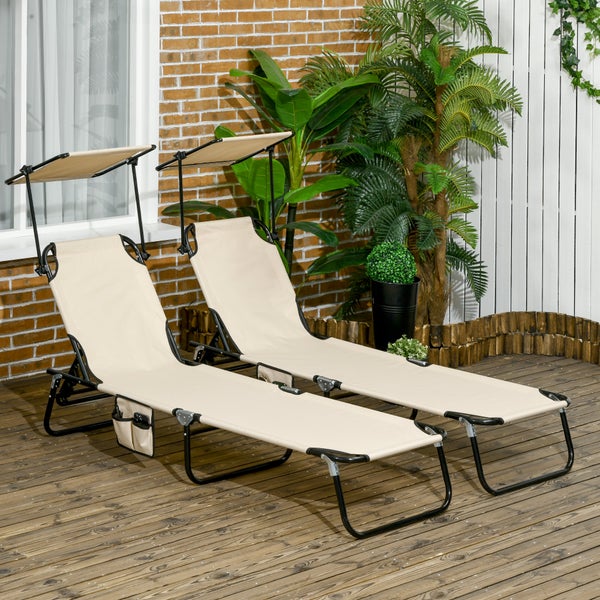 Zwei beige Sonnenliegen mit verstellbarem Sonnendach und Seitentaschen auf einer Holzterrasse vor einer Ziegelwand mit Grünpflanzen.