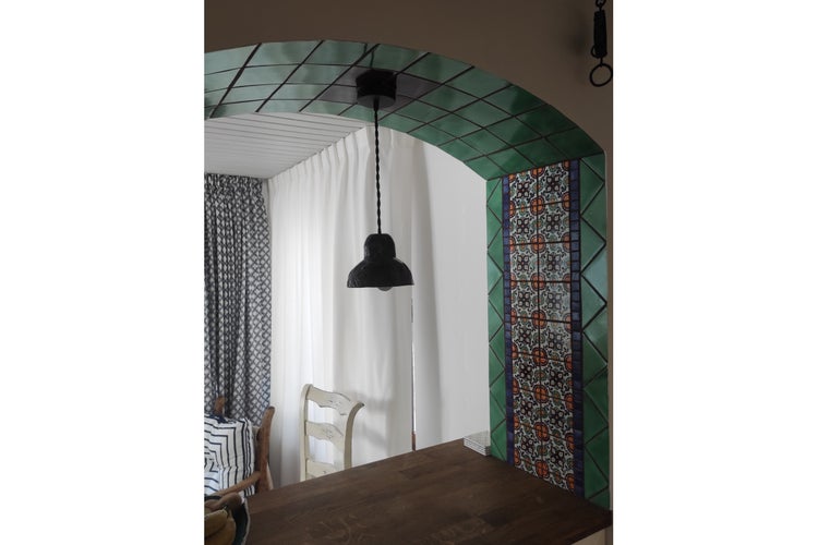 Esszimmer mit Holztisch, Stühlen, Vorhängen und einer Hängelampe über einem Torbogen mit grünen und gemusterten Fliesen.