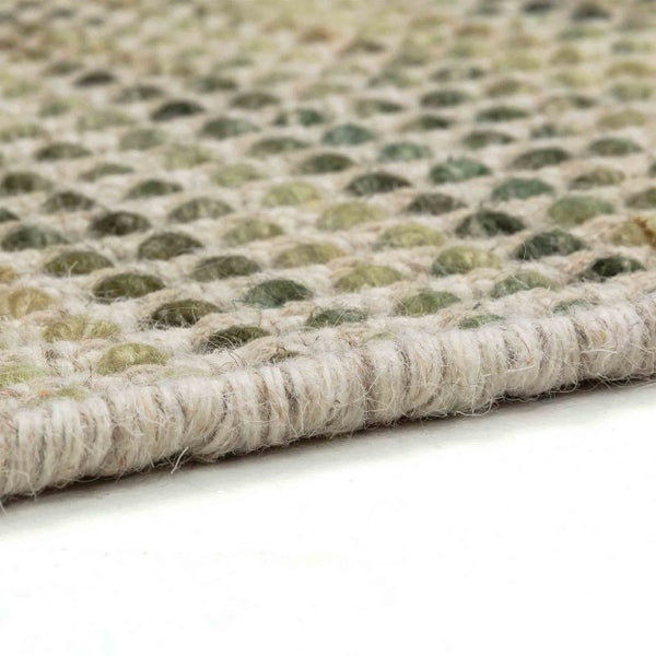 Detailaufnahme eines handgewebten Teppichs mit Noppenstruktur in Grüntönen und heller Kante.