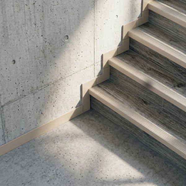 Treppenkantenprofil und passende Treppen-Sockelleiste an Stufen in Holzoptik vor einer Sichtbetonwand.