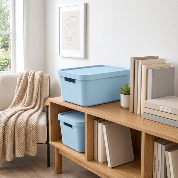 Zwei Kunststoff Aufbewahrungsboxen mit Deckel auf einem Holzregal in einem hellen Wohnzimmer mit Sessel und Büchern