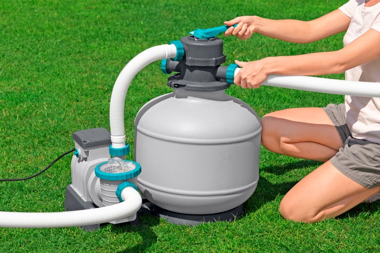 Frau bedient eine Sandfilteranlage für Pools auf einer Rasenfläche