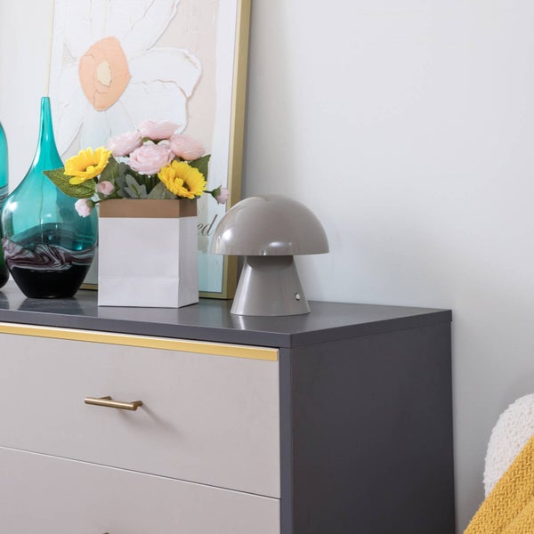 Moderne Kommode dekoriert mit einer pilzförmigen Tischleuchte, einer Glasvase, Kunstblumen und einem gerahmten Bild.