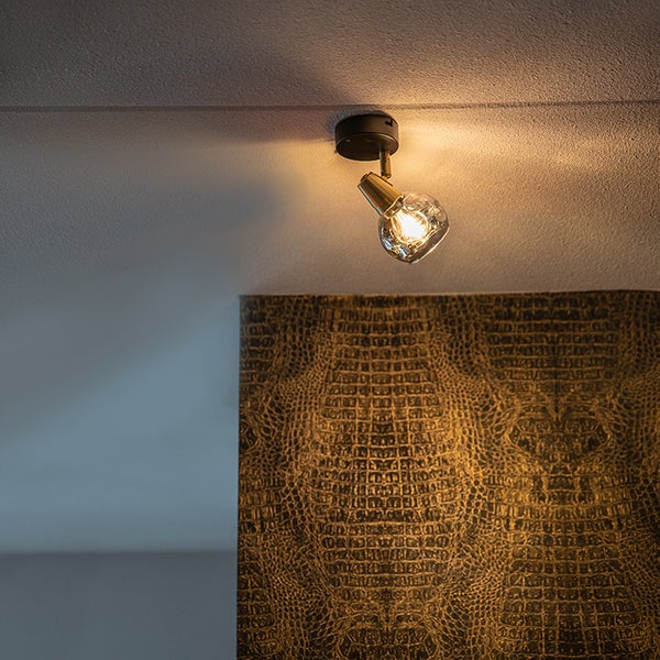 Einflammiger Deckenstrahler aus Messing mit Glasschirm an der Decke montiert, darunter eine Wand mit Tapete in Krokodiloptik.