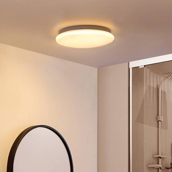 Runde Deckenleuchte mit warmweißem Licht in einem hellen Badezimmer mit Spiegel und Dusche.