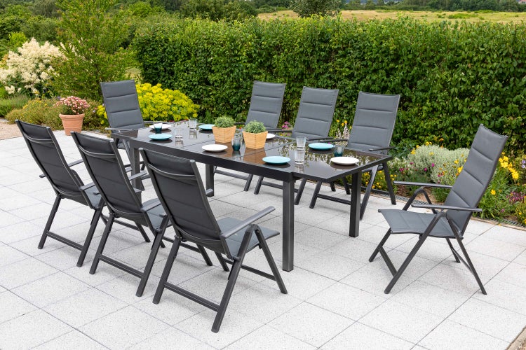 Gartenszene mit Esstisch aus Glas und acht Klappstühlen auf einer Terrasse.