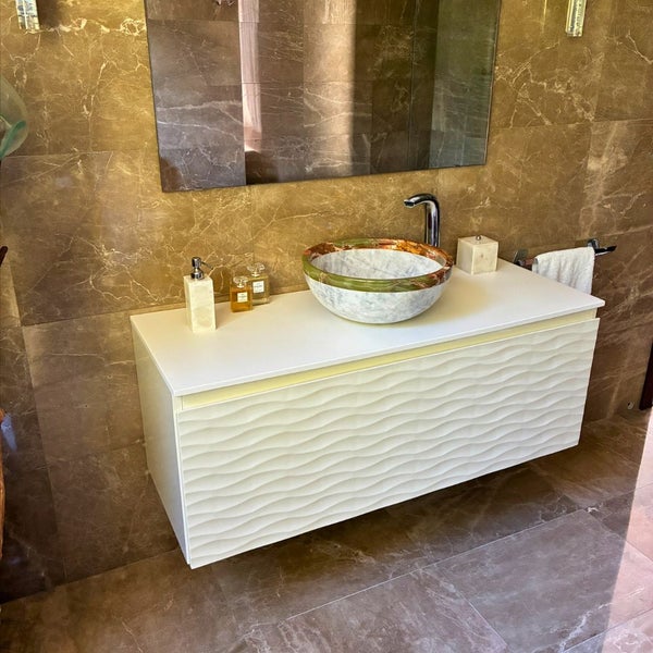 Moderner Waschtischunterschrank mit gewellter Front, Abdeckplatte und rundem Naturstein-Aufsatzwaschbecken vor strukturierter Wand.