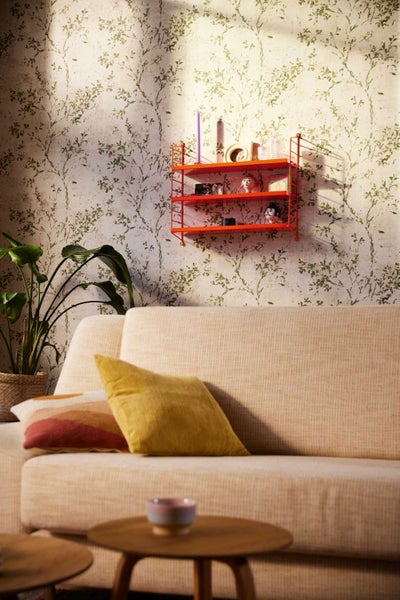Wandregal mit drei Ablagen montiert an einer Tapete mit Pflanzenmuster, platziert über einem Sofa in einem modern eingerichteten Wohnbereich.