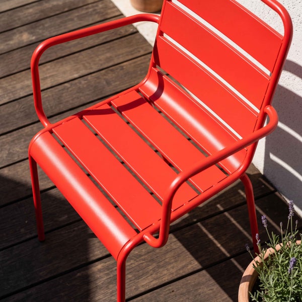 Roter Gartenstuhl aus Metall mit Armlehnen und Lamellen auf einer Holzterrasse.