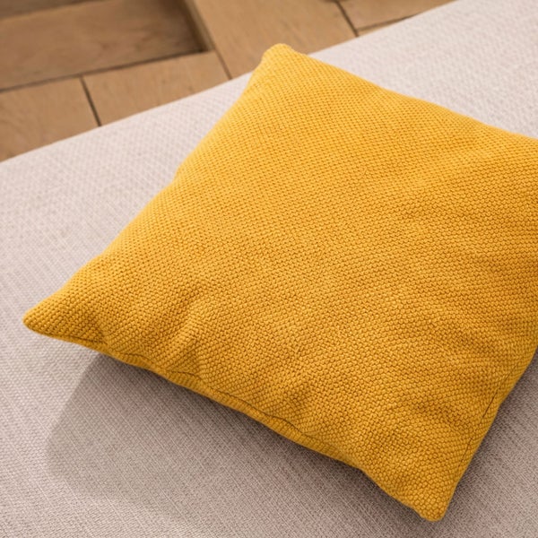 Quadratisches gelbes Kissen auf hellem Stoff