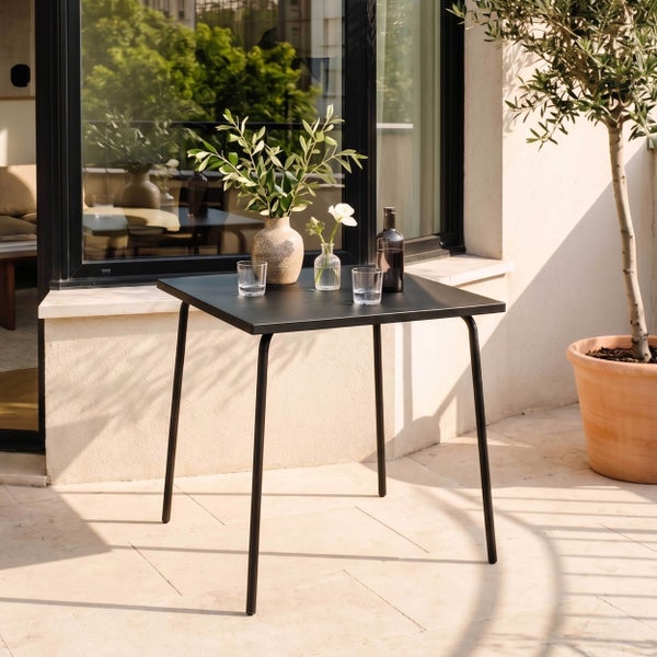 Quadratischer schwarzer Gartentisch aus Metall auf einer sonnigen Terrasse mit Dekoration wie Vasen und Gläsern.