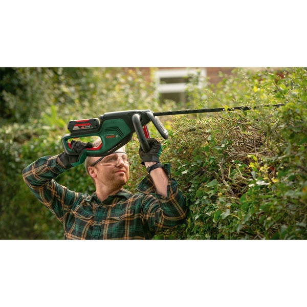 Eine Person schneidet eine Hecke mit einer Bosch Akku-Heckenschere unter Verwendung von Schutzbrille und Handschuhen.