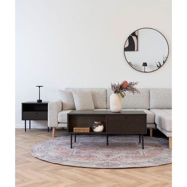 Wohnzimmer-Szene mit grauem Ecksofa, Couchtisch, Beistelltisch, rundem Spiegel und gemustertem Teppich