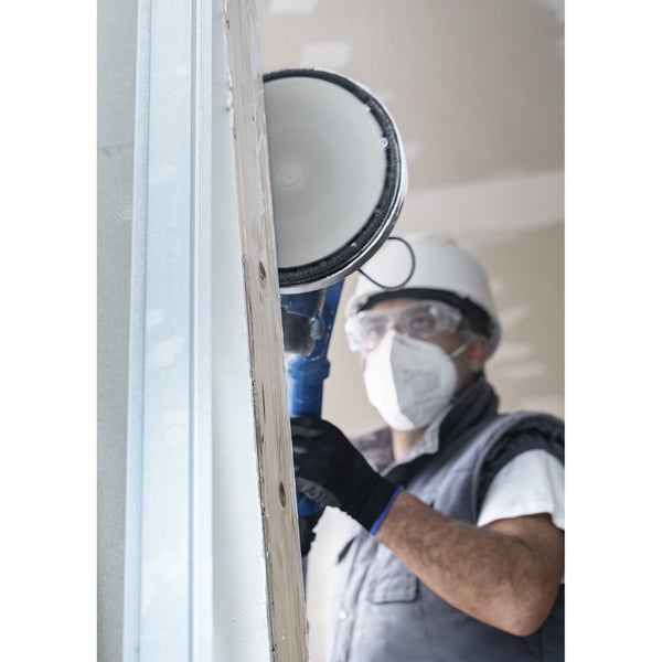 Handwerker schleift eine Holztür mit einem Schleifgerät, während er Schutzkleidung trägt.