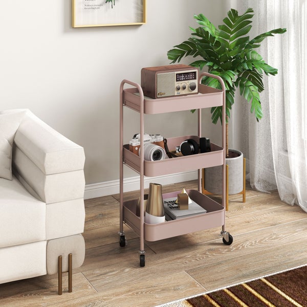 Dreistöckiger Rollwagen aus Metall in Rosa in einem hellen Wohnzimmer neben einem Sofa und einer Zimmerpflanze.