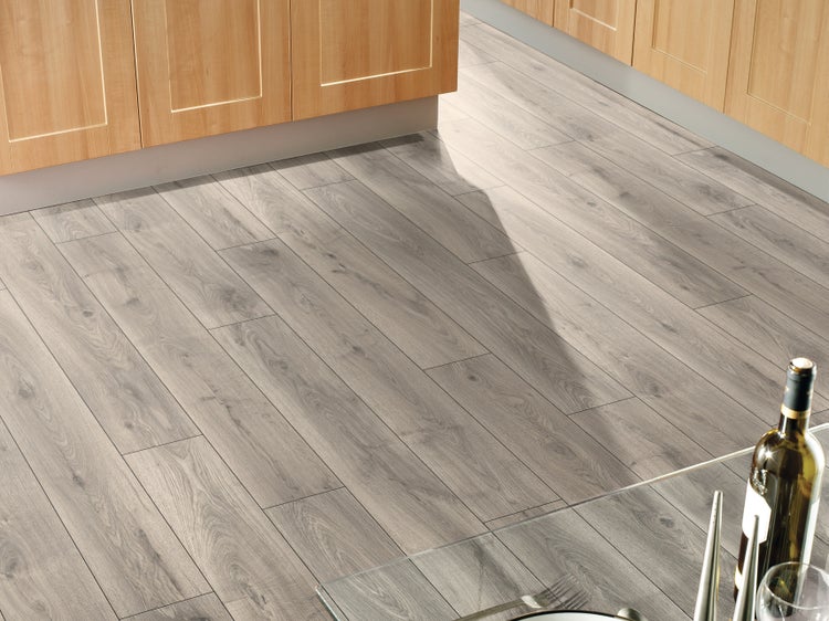 Heller Laminatboden in Holzoptik verlegt in einer Küche mit hellen Holzschränken und einem gläsernen Esstisch.