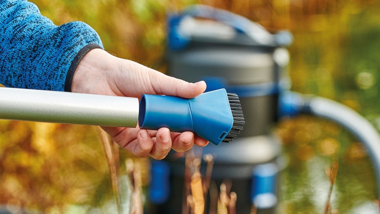 Eine Hand setzt eine Bürstendüse auf das Saugrohr eines Teichsaugers.
