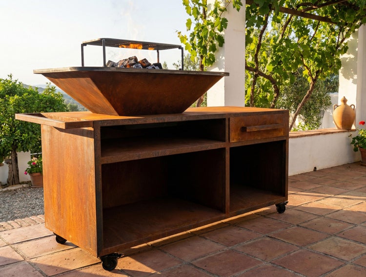 Mobile Outdoor-Grillstation aus Cortenstahl mit Feuerschale, Ablagefächern und Schublade auf einer Terrasse.