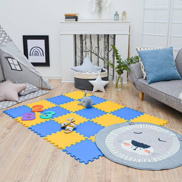 Helles Kinderzimmer mit blau-gelber Puzzlematte aus Schaumstoff auf Holzboden, Spielzelt, grauem Sofa und rundem Löwen-Teppich.