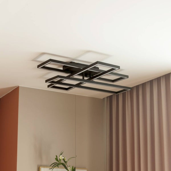 Moderne Deckenleuchte aus Metall mit drei überlappenden rechteckigen Rahmen an der Decke in einem hellen, organisierten Raum mit Vorhang und Pflanze.
