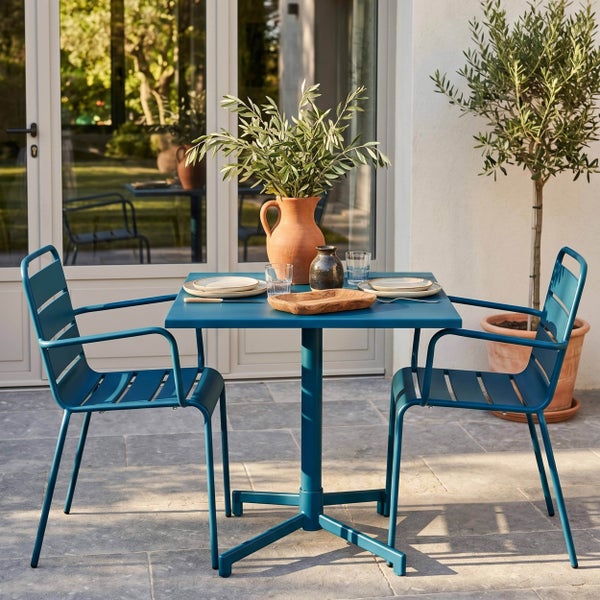Modernes Garten-Set mit quadratischem blauem Metall-Bistrotisch und zwei passenden Metall-Armlehnstühlen auf einer Steinterrasse.