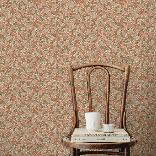 Innenraumszene mit kleinteiliger Blumentapete an der Wand hinter einem Holzstuhl mit Büchern und einem Keramikbecher.