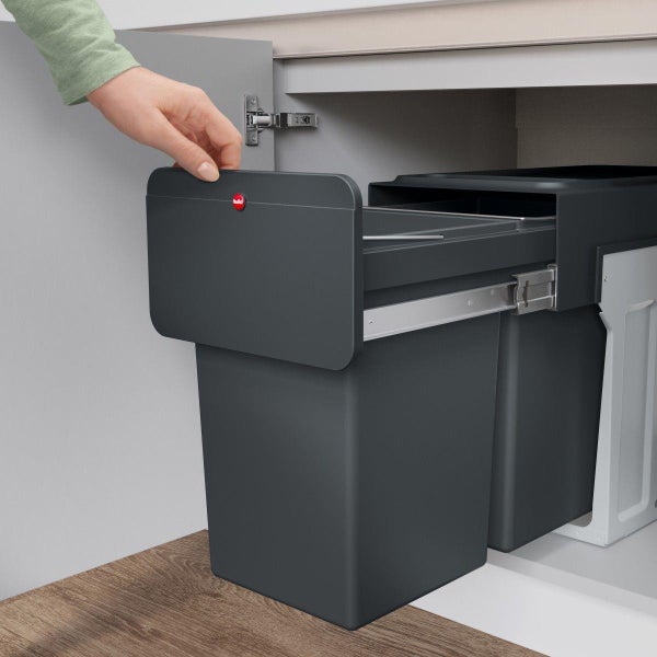Ausziehbares Abfalltrennsystem aus Kunststoff in einem Küchenunterschrank mit einer Hand am Griff. Hailo Logo.