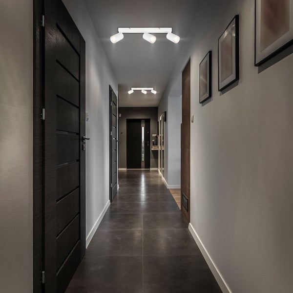 Moderner heller Flur mit weißen dreiflammigen Deckenstrahlern, dunklen Holztüren und anthrazitfarbenem Fliesenboden.