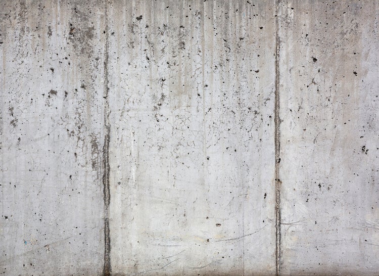 Graue Sichtbetonwand mit vertikalen Fugen und poröser Textur.