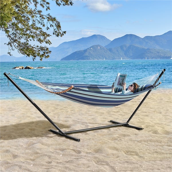 Gestreifte Hängematte mit stabilem Metallgestell und Kissen, aufgestellt am Strand vor einer Berglandschaft.
