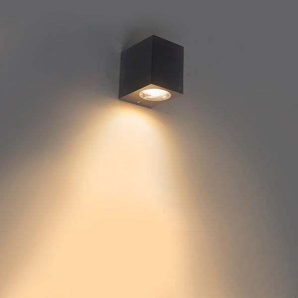 Schwarze, würfelförmige Wandleuchte mit nach unten gerichtetem Lichtstrahl.