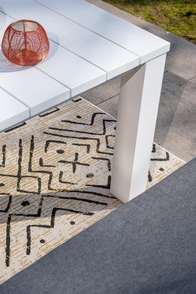 Outdoor-Teppich mit geometrischem Muster unter einem weißen Gartentisch auf einer Terrasse.