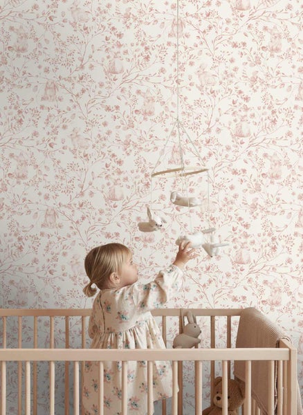 Kindertapete mit einem Muster aus Zweigen, Blüten und Hasen in einem hellen Kinderzimmer mit Holzgitterbett und Mobile.