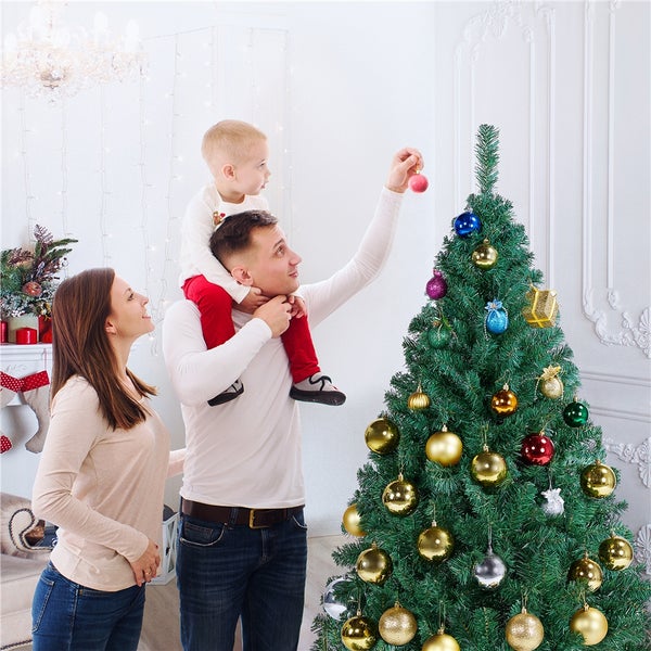 Familie schmückt Weihnachtsbaum mit Christbaumkugeln in einem hellen Wohnzimmer.
