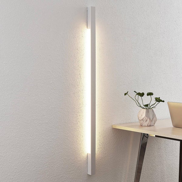 Moderne vertikale LED-Wandleuchte mit indirektem Licht an einer strukturierten Wand neben einem Schreibtisch.