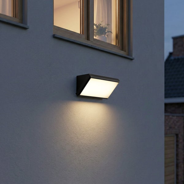 Moderne schwarze rechteckige Außenwandleuchte an einer Fassade unter einem Fenster montiert, Licht strahlt nach unten.