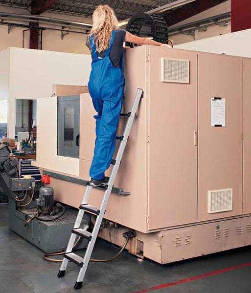 Frau steigt auf eine Aluminium-Stufenleiter in einer Werkshalle.