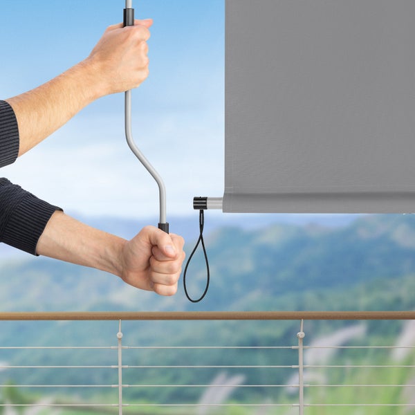 Eine Person bedient eine graue Rollo mit einem Kurbelantrieb auf einem Balkon.