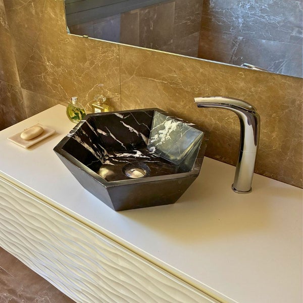 Modernes Bad mit hexagonalem Aufsatzwaschbecken aus dunklem Naturstein, verchromter Armatur und weißem Unterschrank mit Wellenstruktur.