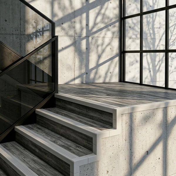 Moderne Treppe mit Stufen in Holzoptik, Sichtbetonwänden und einem Glasgeländer mit schwarzem Rahmen im industriellen Stil.